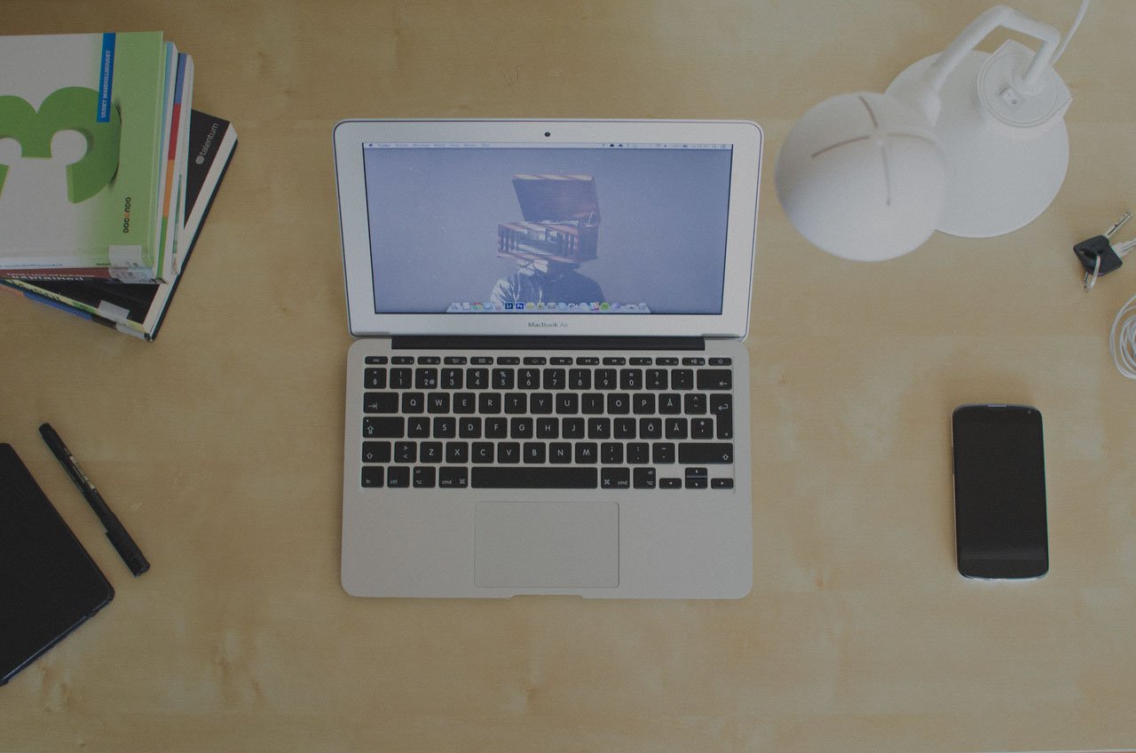 laptop sitting on desk with notebooks, cell phone, and lamp